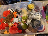 Plastic bin filled with various plush toys including Beanie Babies in different colors and styles.