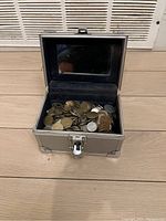 Open metal case showing interior filled with mixed coins