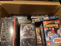 Box filled with assorted DVDs including Lady Death, Hollywood Tough Guys, Thomas & Friends, and various other titles in standard DVD cases.