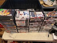 Plastic container filled with stacked PlayStation 2 game cases showing various game titles and cover art arranged on a table