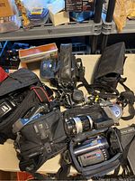 Box with multiple vintage cameras, camcorders, radios, and their carrying cases displayed on a table.
