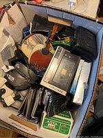 Overview photo of the box showing various electronic items, handheld fans, and cases.