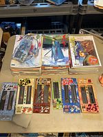 Overall view of lot with stacks of comic books and six boxed miniature weapon decor pieces placed in front.