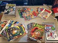Top view showing multiple stacks of comic books featuring Savage Dragon, Shazam, and others spread over a table.