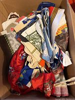 Box containing multiple folded fabric pieces with assorted royal and historic printed designs.