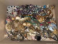 Overhead photo showing large quantity of mixed custom jewelry including bracelets, necklaces, earrings, and brooches in a box.