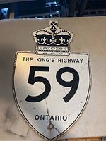 Front view of a shield-shaped metal road sign showing 'The King's Highway 59' with a crown design at the top, signed Ontario, with visible aging marks and wear.