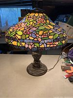 Side angle of the Tiffany style stained glass table lamp showing colorful floral glass pieces on the shade and decorative metal base.