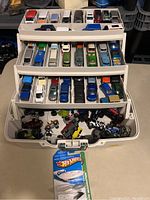Full view of 3-tiered white plastic carrying case filled with multiple trays of vintage Hot Wheels cars and one carded Hot Wheels item in front