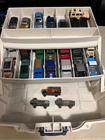 Top view of white plastic storage box containing 19 vintage Hot Wheels die-cast cars and trucks organized in compartments.