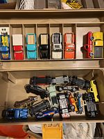 Storage box showing die-cast cars arranged in top tray with separate compartments and loose cars in bottom compartment