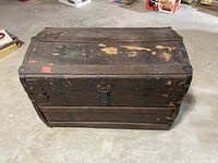 Front view of closed wooden camelback steamer trunk showing worn wood and metal lock latch
