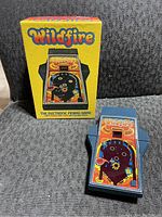 Front view of handheld game and original box showing Wildfire pinball artwork and condition