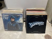 Two stacks of vinyl records with visible front covers of Paradise Alley and Superman The Movie soundtracks.