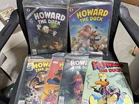 Six 1980's Howard The Duck comic books displayed on black chair, each individually bagged in clear plastic, showing colorful vintage comic cover art.