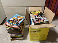 Two stacks of comic books, one on the floor and one inside a repurposed cat litter box