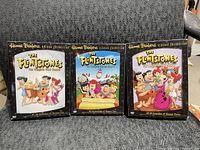 Photo of three DVD box sets of The Flintstones Seasons 1, 2, and 3 with distinctive artwork and titles on the front.