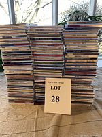 Full view of stacked lot of 100 music CDs on table showing front edges and general condition.
