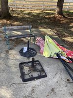 Wide photo showing the child-sized wood and metal bench, two metal umbrella holders, and the folded patio umbrellas on the ground