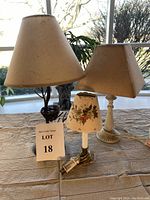 Photo showing three vintage lamps with different style bases and shades on a table in front of a window.