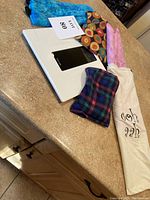 Four microwavable heating pads with varied fabric patterns and a white fabric pouch with text, plus a Taylor digital scale on countertop.