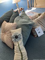 View of the pillows arranged on the bedspread shows variety of colors and textures including ribbed corduroy, striped beige with piping, and a flower accented pillow.
