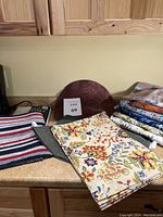 Countertop with 7 textile items including colorful patterned tablecloths, runners, and place settings