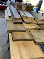 Stack of hardwood barn wood boards laid on a table, showing variation in thickness and width, rough edges visible.