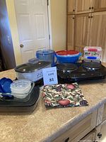 Overview of the lot showing 2-burner electric grill, slow cooker, storage containers with blue lids, ice bucket, and decorative kitchen towel on countertop