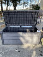 Front view of the large dark gray plastic storage chest with the hinged lid open, showing outer textured panel design and size.