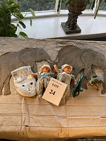 Photo of two metal elephant wall decorations, two baby dolls in striped outfits and hats, a white bear hand puppet, and plastic whale and frog toys on a table with a lace cloth.