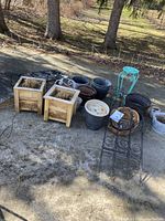 Photo showing all items in lot grouped on outdoor concrete surface, including two wooden planters, several plant pots, metal stands, and garden fences.
