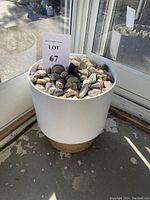 Photo of a white round gas fire bowl planter filled with natural rocks and a central black knob, next to a window.