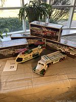 Overview of six Hess collectible vehicles and their original display boxes on a table, showcasing the variety of trucks, helicopter, and trailers.