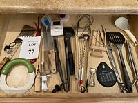 Top-down view of a kitchen drawer filled with various utensils including peelers, tongs, wooden-handled knives, a timer, graters, and spatulas.