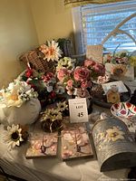 Group photo showing various handmade floral home decor items arranged on a table, including flower arrangements, baskets, plaques, and containers in soft pastel and natural colors.