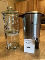 Photo of large clear glass beverage dispenser next to GE stainless steel coffee maker with lid and spout, both placed on kitchen counter.