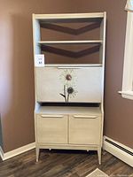 Full view of mid-century modern room divider hutch with secretary desk and floral painting on drop-front desk panel.