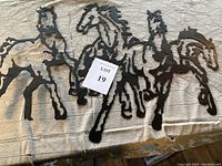 Full view of the metal horse artwork showing three abstract horses on a textured fabric background with a lot label.