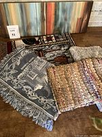 Overview photo showing modern abstract canvas print behind four different throws laid out in front on a wooden surface.