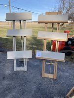 Four adjustable hand made craft display units with white shelves and wooden frames shown outdoors on pavement. Each unit has three horizontal shelves, adjustable and foldable design.