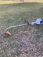 Full length view of the STIHL FS 40 weed wacker laid on grass showing the orange guard, cutting end, and engine housing.