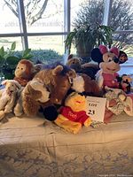 Lot of 8 stuffed animals including character dolls and animals arranged together on table with window background