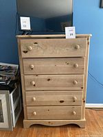 Full frontal view of the tall dresser showing four drawers, wood knob handles, and floral decorative detail on the top drawer.