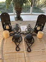 Full view of both metal wall sconces, curved metal holders, glass hurricanes, two tan pillar candles and three small white candles on lace cloth background.