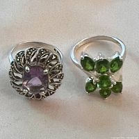 Photo of two silver rings side by side on fabric background, showing amethyst and green gemstone rings