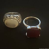 Top view of two sterling silver rings, left with an oval white stone and tribal scroll designs and right with a square red stone.