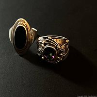 Two tribal style rings, one with oval black stone and the other with a multicolor faceted gem with ornate silver detailing, photographed on black background.