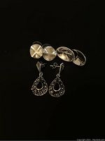 Photo showing the three pairs of sterling silver earrings on a black background: round brushed studs, oval concave studs, and teardrop drop earrings.