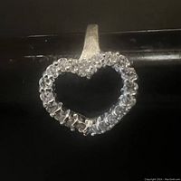 Close-up of silver open heart ring with clear rhinestones on black surface showing ring detail and texture